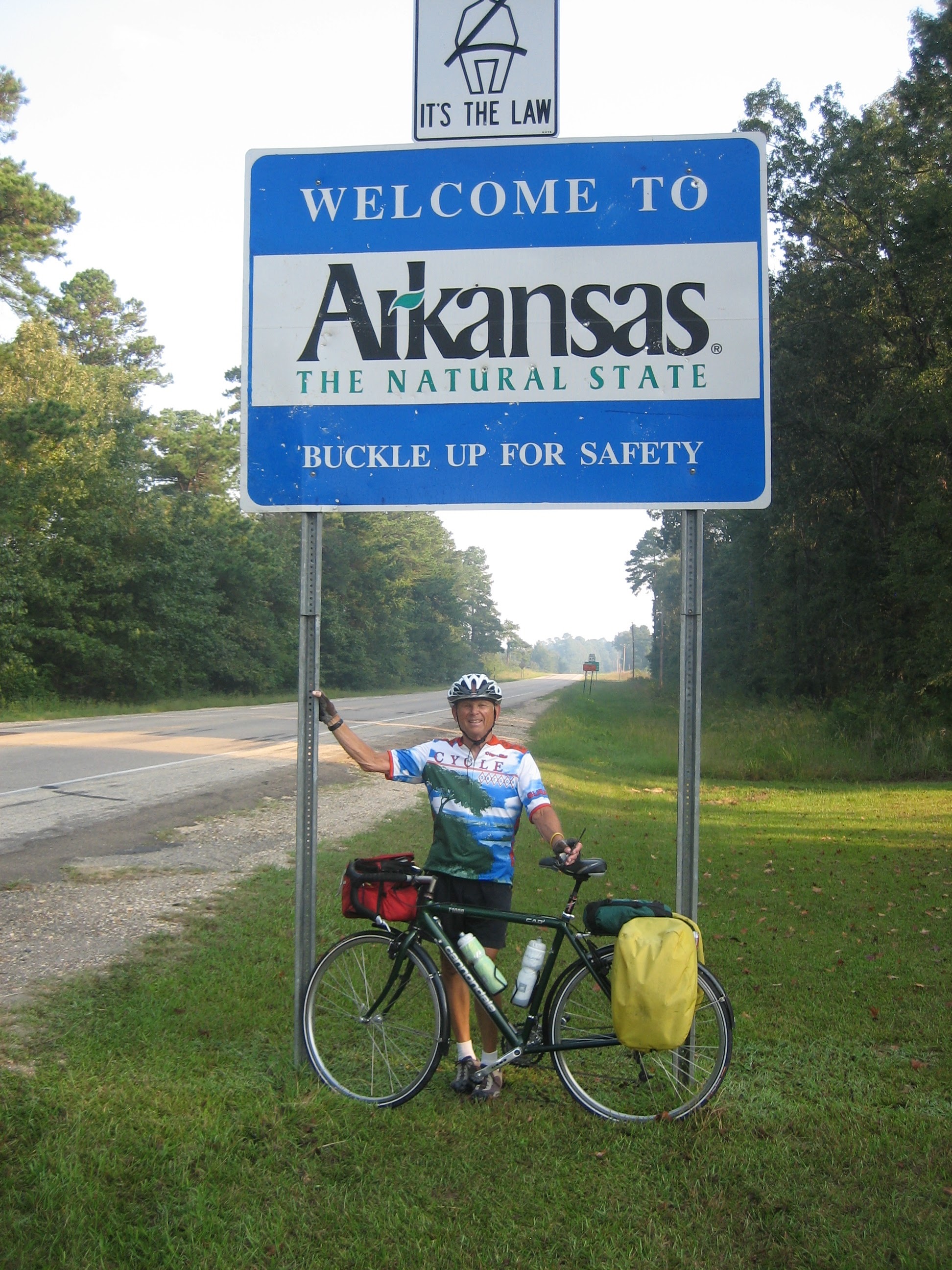 Tom or his touring bicycle photographed at the Arkansas state line or state landmark.
