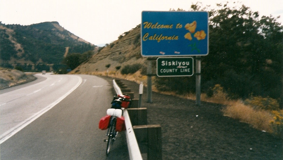Tom or his touring bicycle photographed at the California state line or state landmark.